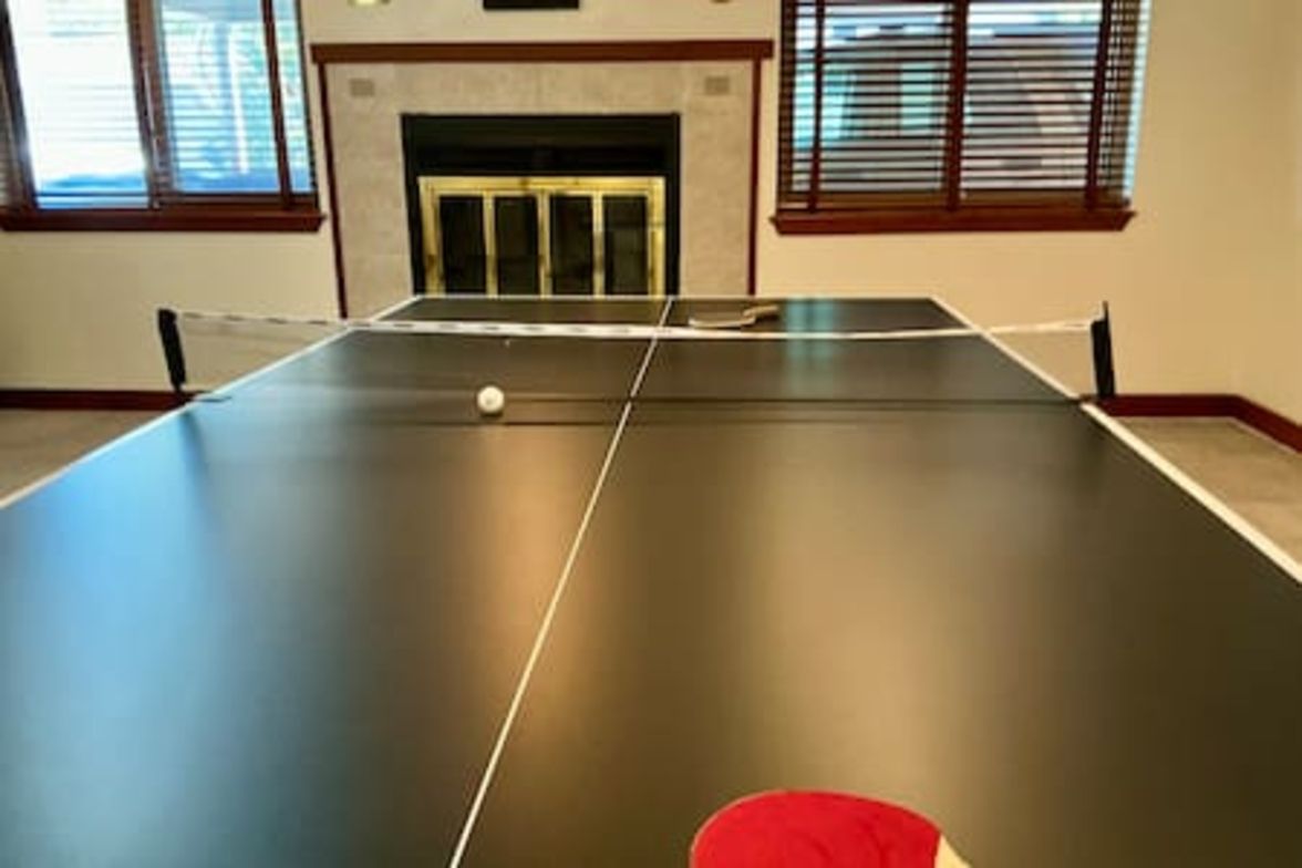 A ping pong table with a net in a room with a fireplace and windows.