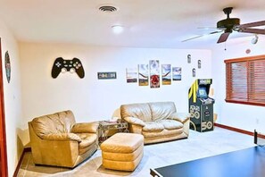 A living room with two leather sofas, a coffee table, a ceiling fan, and a retro arcade machine. - FW Pool + Arcade - Fun Near TX Speedway (Fort Worth)