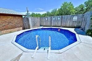 Et rektangulært swimmingpool med en stige i midten, omgivet af et træhegn og en murstensmur.