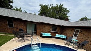 Ein rechteckiger Swimmingpool mit integrierter Leiter, umgeben von einer Ziegelterrasse mit Gartenmöbeln.