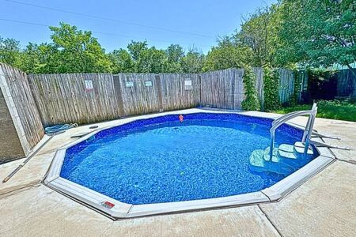 Une piscine entourée d’une clôture en bois, avec une échelle et une terrasse carrelée.