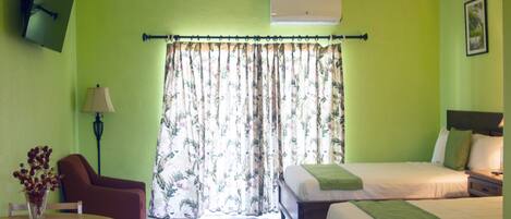 Une chambre d’hôtel avec un lit, une chaise, une table ornée d’un vase de fleurs et un ventilateur de plafond.