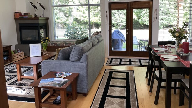 Uma sala de estar ampla com lareira, um sofá, uma mesa de centro e um espaço de jantar com mesa posta para dois.