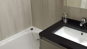 Un baño con una bañera blanca, un lavamanos con encimera negra y un espejo.