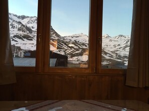 A room with a large window offering a view of snow-covered mountains and buildings. - Nice 3 room apartment on the 2nd floor, south facing, mountain / resort view (VAL THORENS)