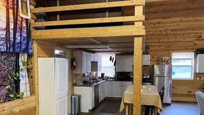 A rustic cabin interior with a kitchen area, wooden walls, and a loft space. - The Hruby Doobie Doo Ranch (Crown Point)