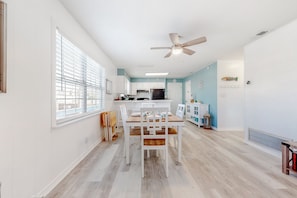 A spacious kitchen with white cabinets, a dining table with chairs, and a ceiling fan.