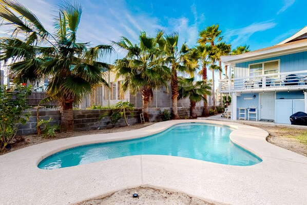 A swimming pool with a curved edge, surrounded by palm trees and a house with a balcony.
