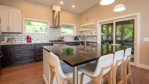 Une cuisine moderne avec un îlot central, des meubles de couleur sombre et des chaises blanches.