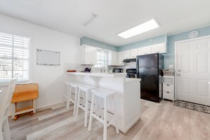 A modern kitchen with white cabinetry, a black refrigerator, and a bar area with white stools.