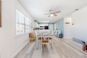 A modern kitchen with white cabinets, a dining area with a wooden table and chairs, and a ceiling fan.