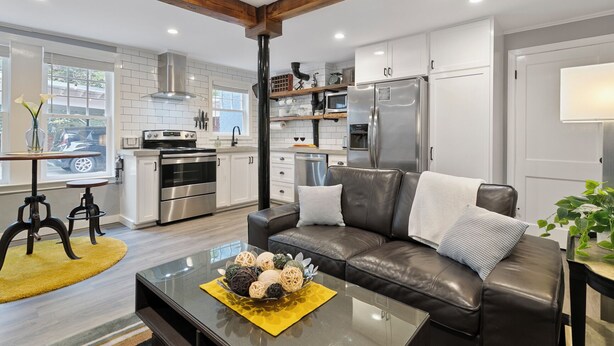 A modern kitchen with stainless steel appliances, a dining area with a leather couch, and a view of the street through large windows. - Belhaven Arts Hideaway: Private Suite + Walkable (Jackson)