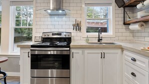 A kitchen with white cabinetry, a stainless steel stove, and a window with a view of greenery. - Belhaven Arts Hideaway: Private Suite + Walkable (Jackson)