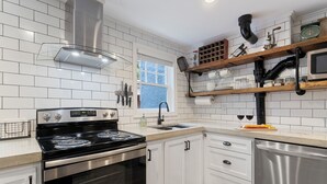 A modern kitchen with white cabinetry, stainless steel appliances, and a wooden shelf with various items. - Belhaven Arts Hideaway: Private Suite + Walkable (Jackson)