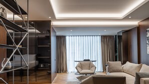 A modern living room with a sofa, armchair, and a glass shelving unit. - Hotel MANAMI (Pristina)
