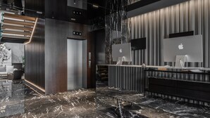 A modern reception area with marble flooring, wooden accents, and Apple iMacs on the desk. - Hotel MANAMI (Pristina)