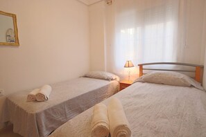 A hotel room with two single beds, a nightstand with a lamp, and a framed picture on the wall. - 053 - Altomar II 003 - comfortHOLIDAYS (Santa Pola)