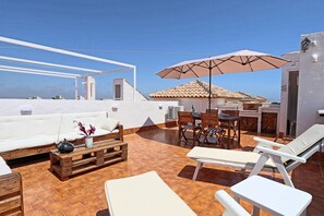 A rooftop terrace with a white sofa, wooden dining table, and lounge chairs. - 053 - Altomar II 003 - comfortHOLIDAYS (Santa Pola)