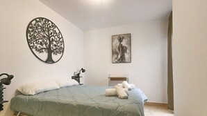 Et soveværelse med en seng, et træ på væggen, et billede og et sengebord med en lampe.