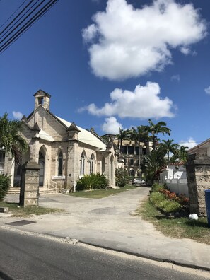 A historic church with a bell tower and arched windows, surrounded by palm trees and a paved road.