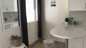 Une cuisine avec un plan de travail rond et blanc, un petit tabouret, une plante en pot et un élément décoratif fixé au mur.
