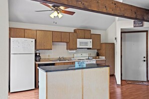 A kitchen with wooden cabinets, a white refrigerator, a microwave, a stove, and a sign that reads 'Boats Well with Others.'