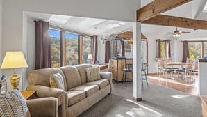Un amplio espacio habitable con sofá, mesa de comedor y sillas, ventanas grandes con vistas y un ventilador de techo.
