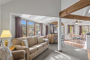 Un amplio espacio habitable con sofá, mesa de comedor y sillas, ventanas grandes con vistas y un ventilador de techo.