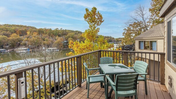 A deck with a table and chairs overlooking a lake with boats, surrounded by autumn foliage.