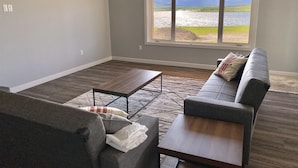 Een ruime woonkamer met een groot raam dat uitzicht biedt op een meer en bergen.