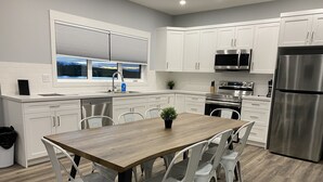 Een moderne keuken met witte kastjes, roestvrijstalen apparatuur, een houten eettafel en witte stoelen.