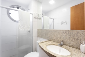 A modern bathroom with a granite countertop sink, a glass shower enclosure, and a white toilet. - OKA BEACH RESIDENCE Porto de Galinhas (Ipojuca)