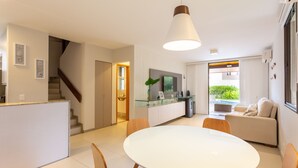A modern kitchen with a glass island, white cabinets, and a dining area with a round table and wooden chairs. - OKA BEACH RESIDENCE Porto de Galinhas (Ipojuca)