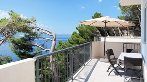 A balcony with a table and chairs, a large umbrella, and a view of the sea and trees. - Vacation home Lada by Interhome (Omiš)