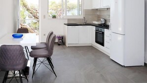 A modern kitchen with white cabinets, a black countertop, and a built-in oven. There is a dining area with a table and chairs, and a window providing a view of the outdoors. - Vacation home Lada by Interhome (Omiš)