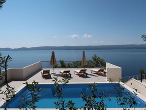 A rooftop pool with lounge chairs and umbrellas overlooking a large body of water. - Vacation home Lada by Interhome (Omiš)
