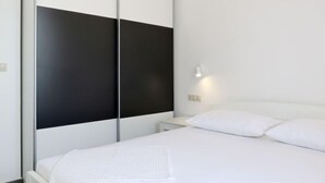 A modern bedroom with a bed, white bedding, a nightstand, and a wardrobe with a black panel. - Vacation home Lada by Interhome (Omiš)