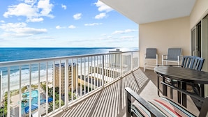 A balcony with a view of the ocean, a pool, and a dining area with chairs and a table. - Crystal Tower 1603, Gulf views/ 3 Pools/King Bed (Gulf Shores)