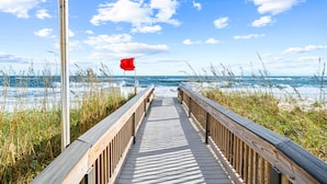 A wooden boardwalk leading to the beach with a red flag and ocean waves in the background. - Crystal Tower 1603, Gulf views/ 3 Pools/King Bed (Gulf Shores)