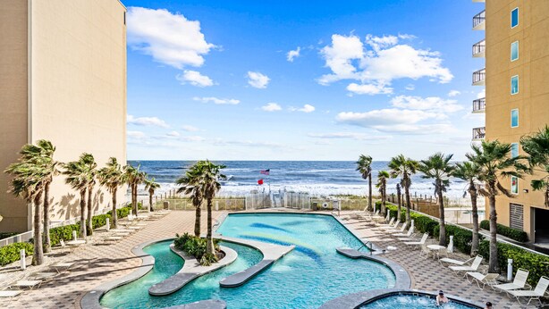 A swimming pool with a view of the ocean, surrounded by palm trees and lounge chairs. - Crystal Tower 1603, Gulf views/ 3 Pools/King Bed (Gulf Shores)