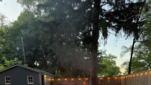 Un patio trasero con un pozo de fuego circular, dos sillas Adirondack y un cobertizo pequeño.