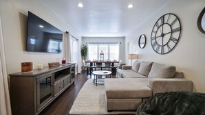 Una sala de estar con televisor, sofá, mesa de centro y un comedor con mesa y sillas.