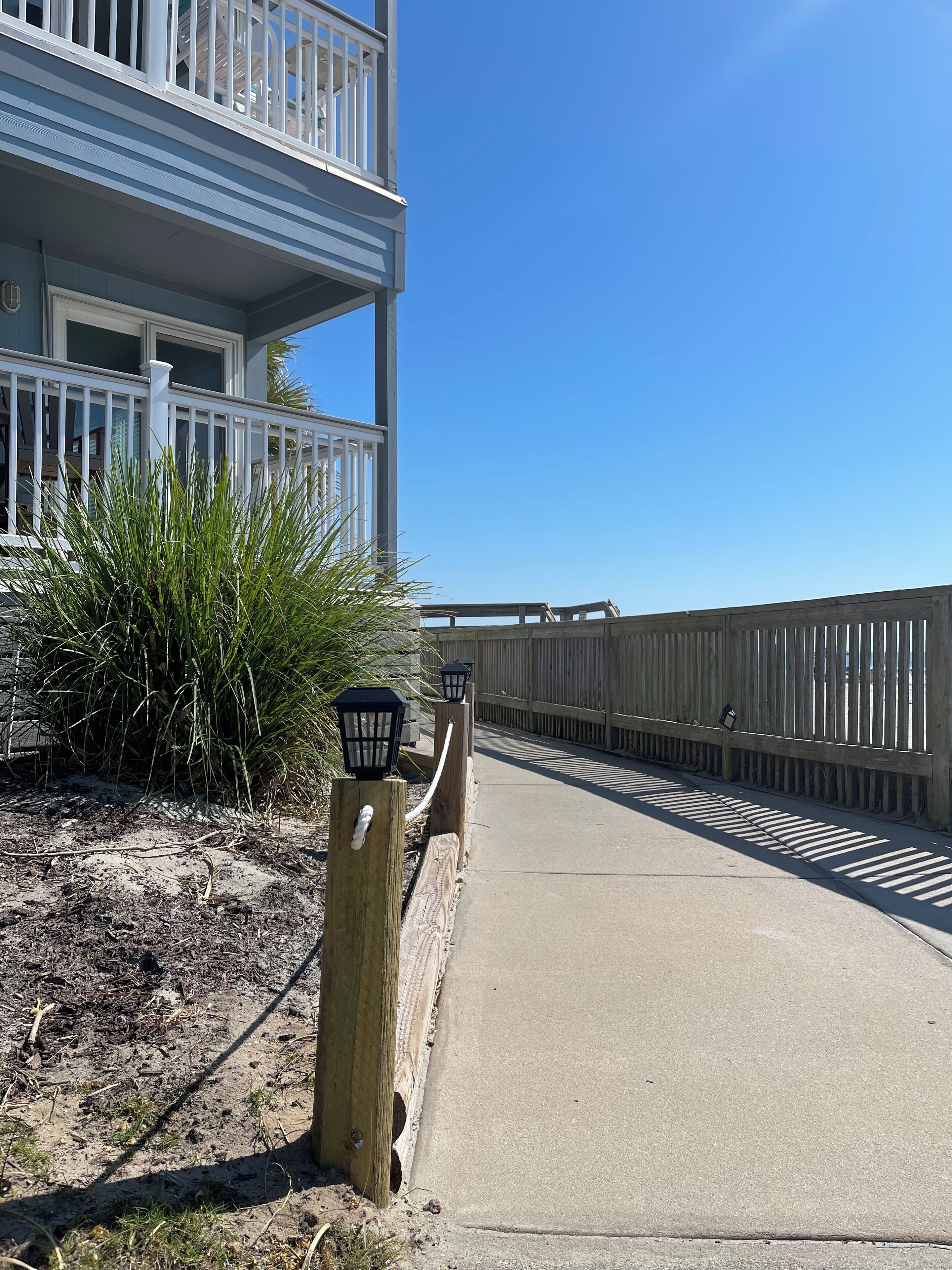 A coastal walkway with a wooden fence, a concrete path, and a building with a balcony.