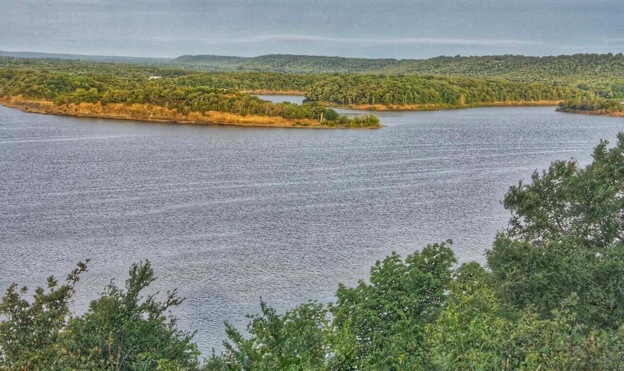 Une vaste étendue d’eau entourée d’une végétation luxuriante, avec des collines en arrière-plan.