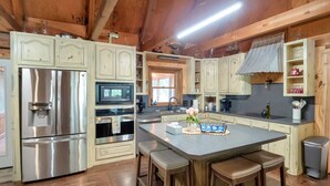 A kitchen with wooden cabinets, stainless steel appliances, a central island with stools, and a window above the sink.