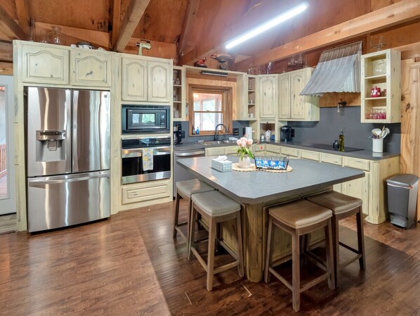 A kitchen with wooden cabinets, stainless steel appliances, a central island with stools, and a window above the sink.