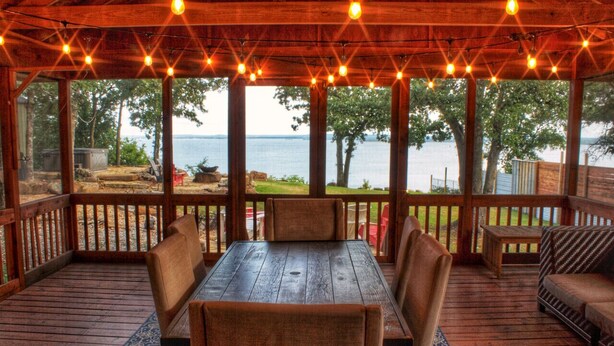 A wooden deck with a table and chairs, overlooking a body of water.