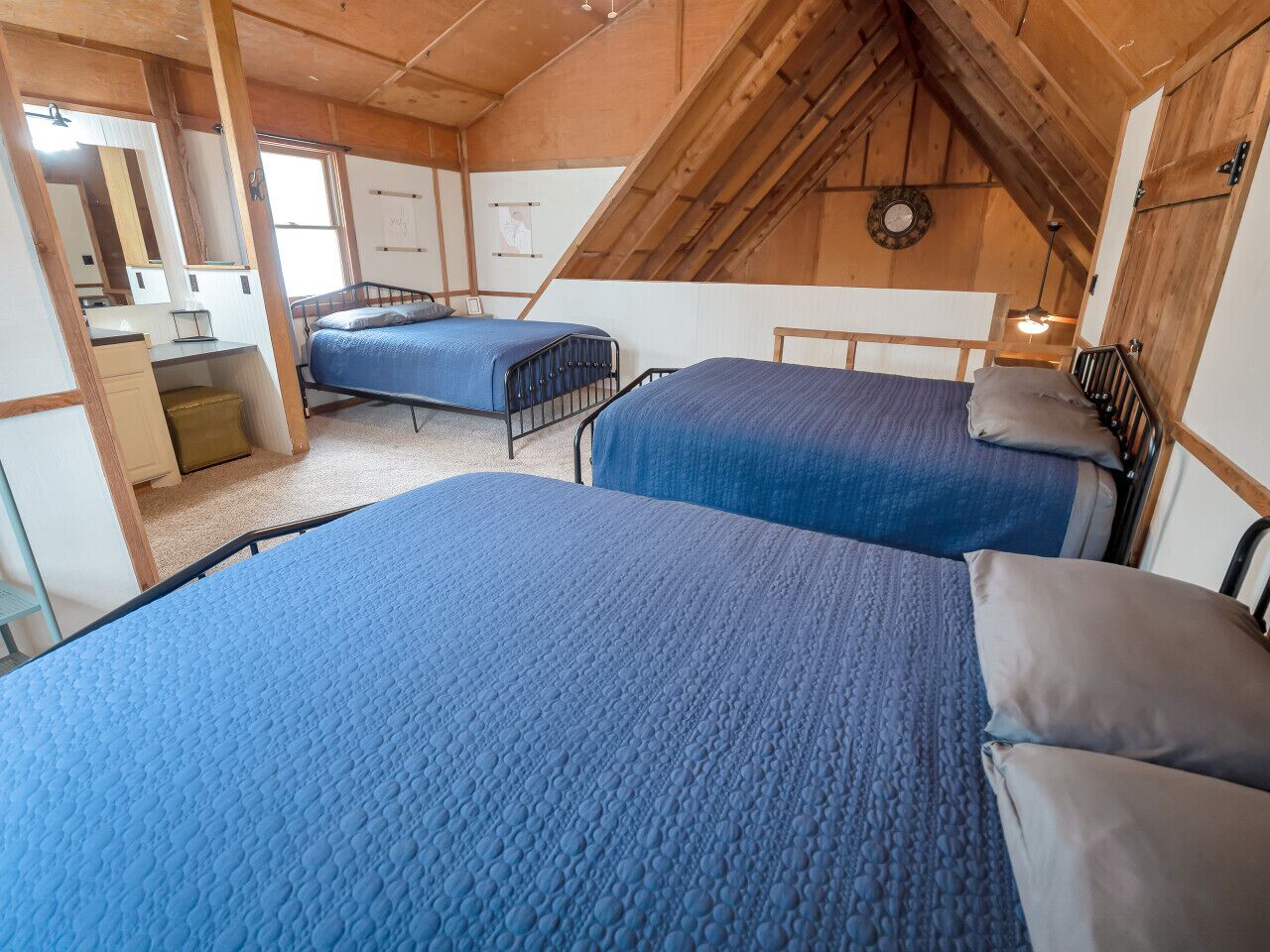 A cozy attic bedroom with two beds, wooden beams, and a small desk area.