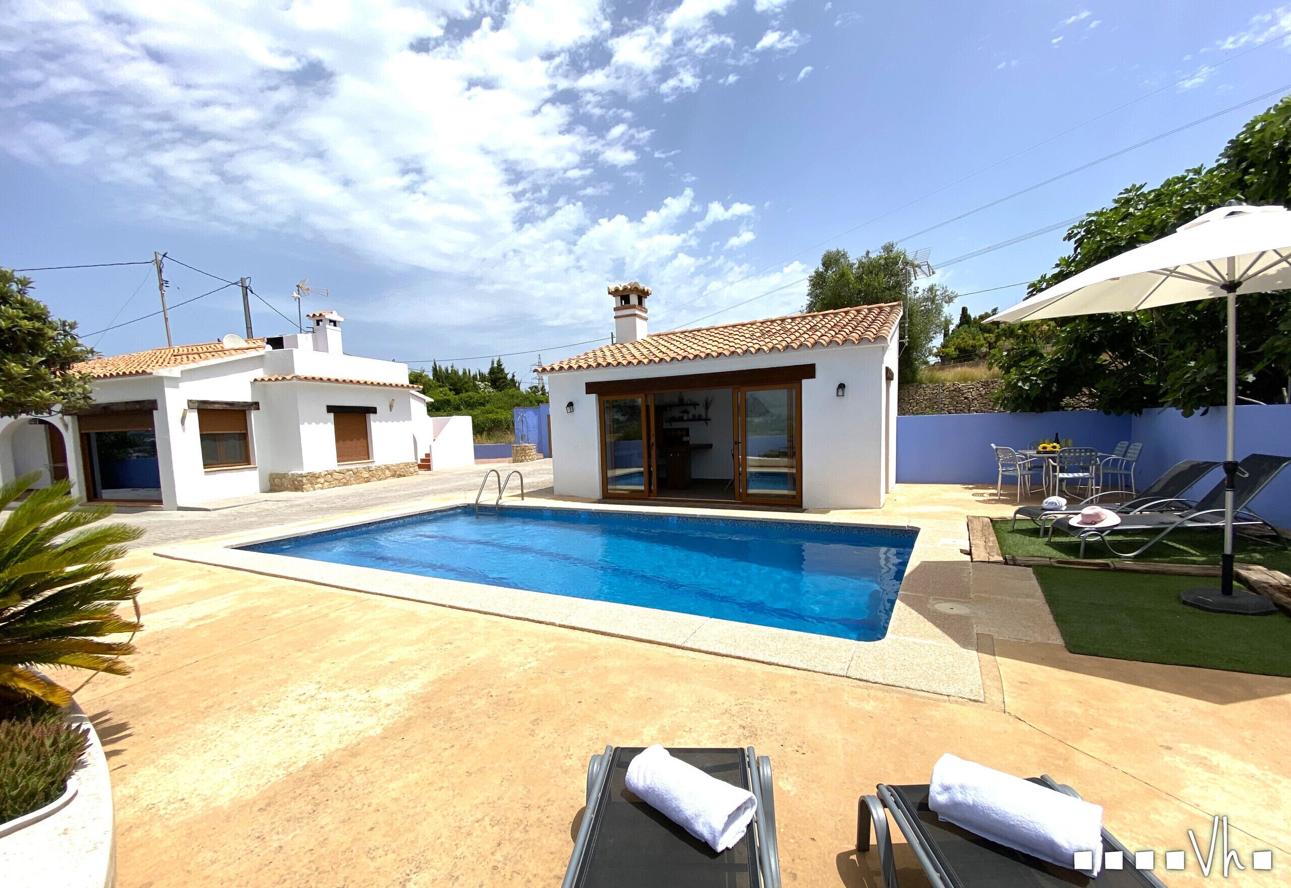 A swimming pool with lounge chairs and a small building with a tiled roof.