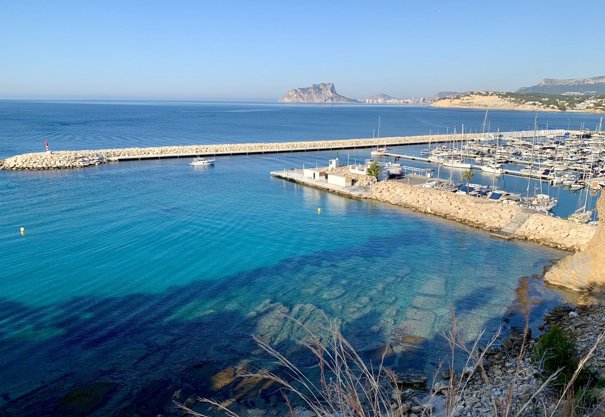 Un port de plaisance avec des bateaux amarrés, une eau d’un bleu limpide et une côte rocheuse.